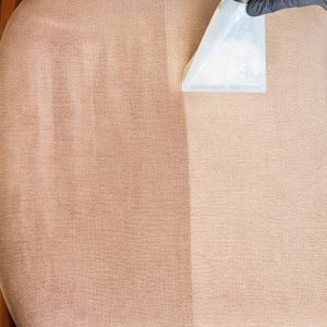 Fotografia vista de cima detalhando a limpeza de cadeiras estofadas em BC. Uma ferramenta extratora transparente remove a sujeira de um assento bege, criando um nítido contraste de "antes e depois" entre a metade limpa e clara recém-lavada, e a área ainda escura e encardida. O técnico utiliza luvas pretas para manipulação segura do equipamento.